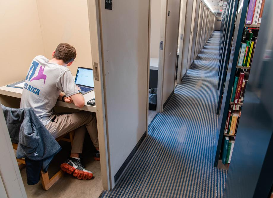 A row of rooms without doors with a student studying in the one closest to the camera.