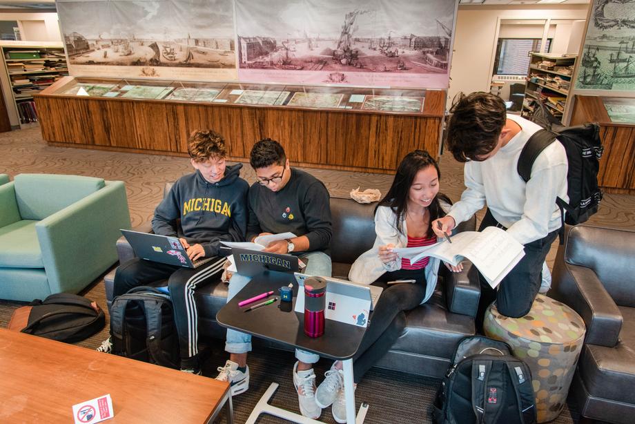 Students sitting together and talking with a map exhibit in the background.