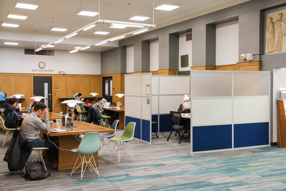 Students sitting at tables with colorful chairs and space with partitions. 