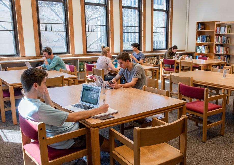 Open space with windows and students scattered, sitting around large wooden stables.