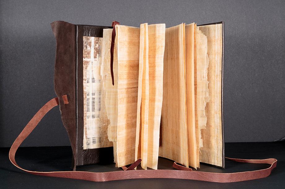 An open book standing on a table with pages fanned out and a visible leather cover with a tie.