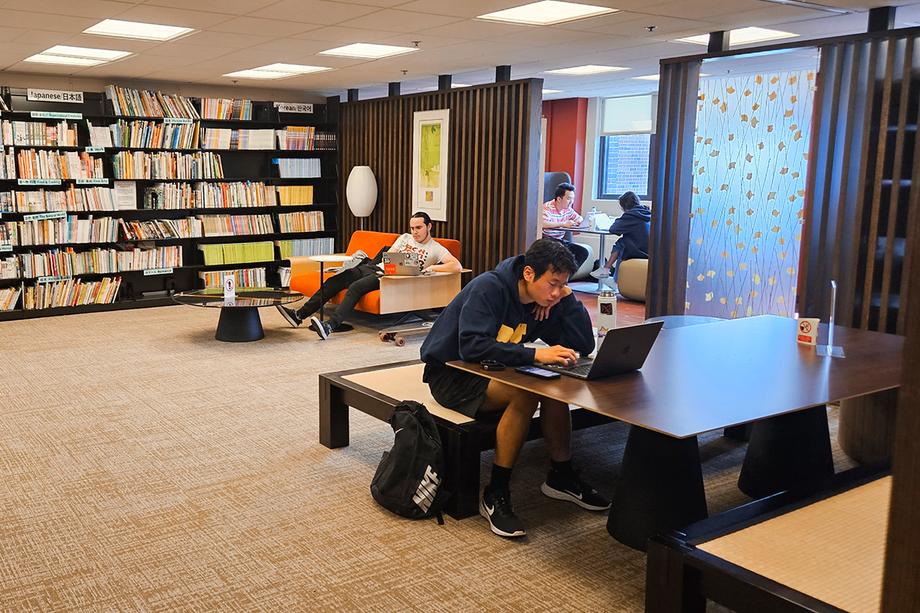 Students using seating in the Tadoku Room with laptops and booths in the background