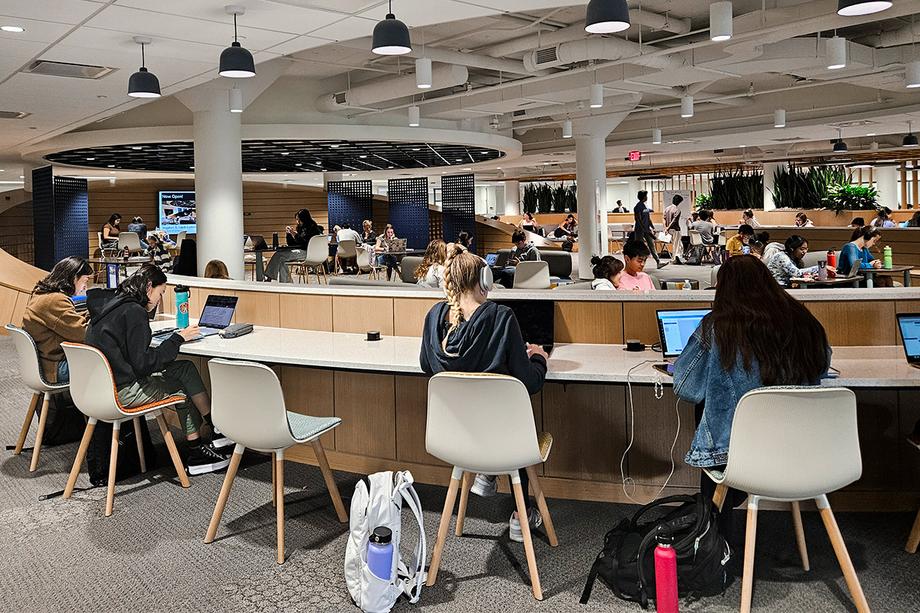 A view of the Clark Commons Living Room with students along counter seating in foreground and seated throughout the space