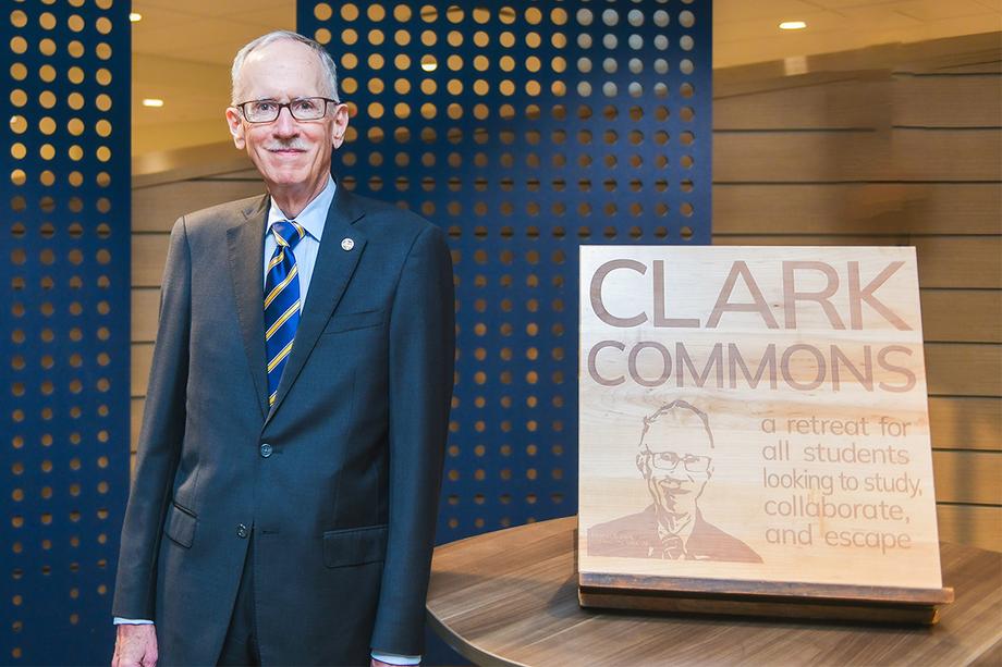 Stephen Clark smiling next to a wood plaque dedicated to him. 