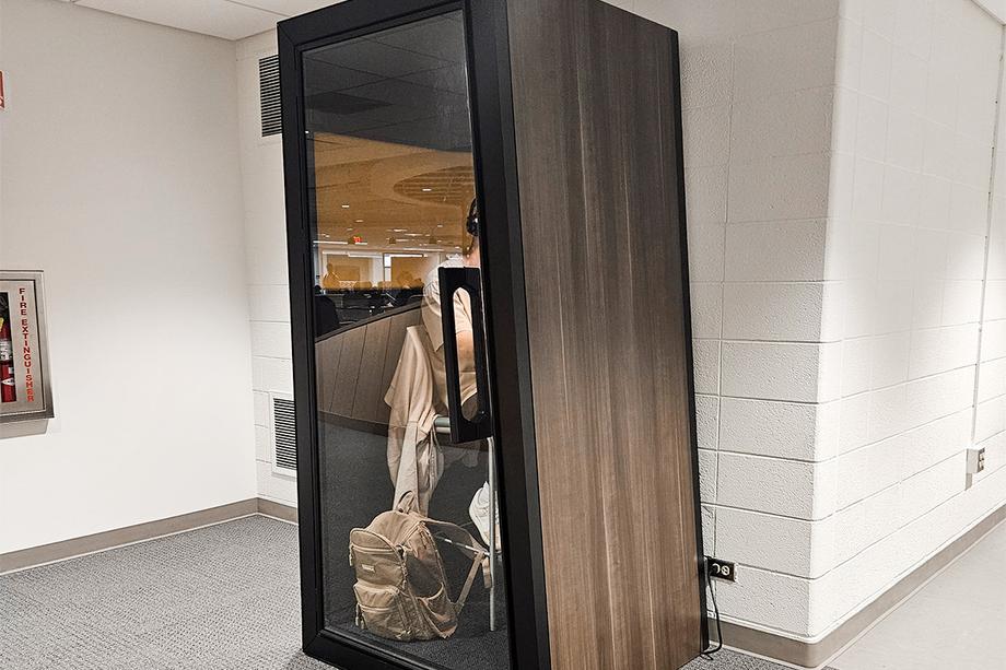 Student seated inside a tall soundproof booth with a transparent door