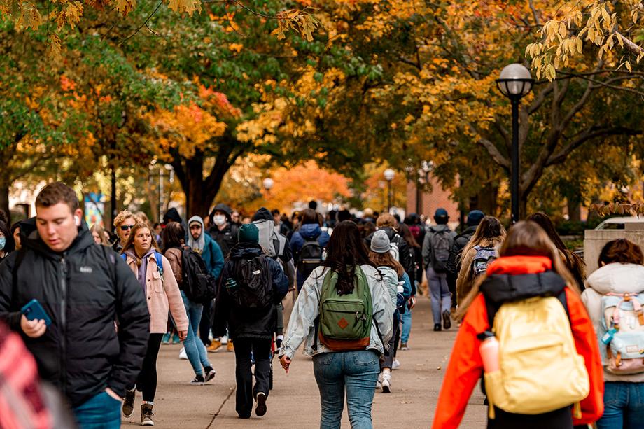 People walking in either direction on a Diag walkway with trees in fall color all around.