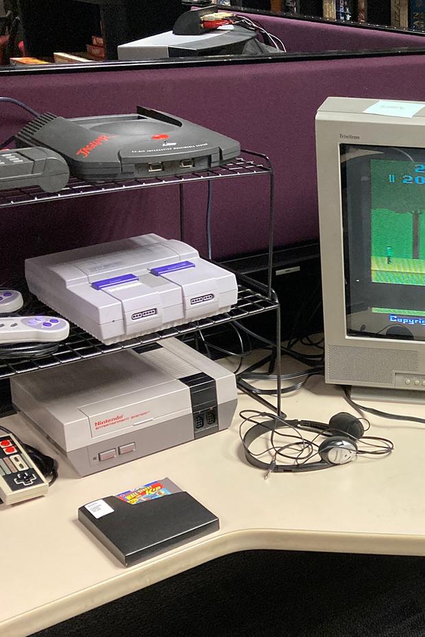 Wireshelving with an original Nintendo and other game systems next to older computer monitor.